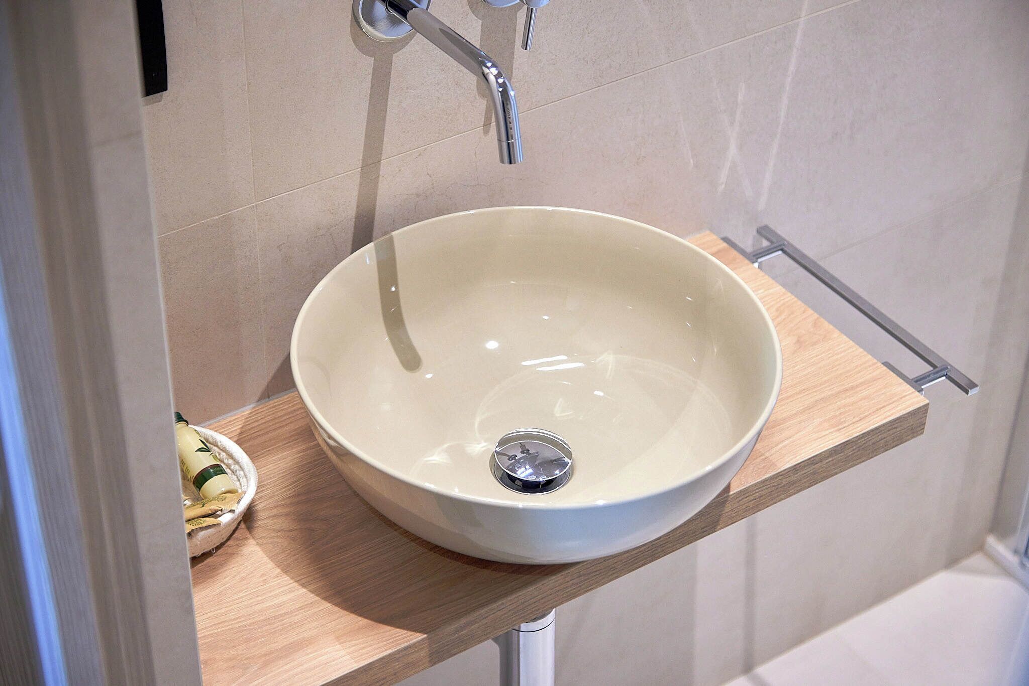 Une salle de bain avec un lavabo blanc posé sur une étagère en bois, un robinet et des toilettes visibles au fond.