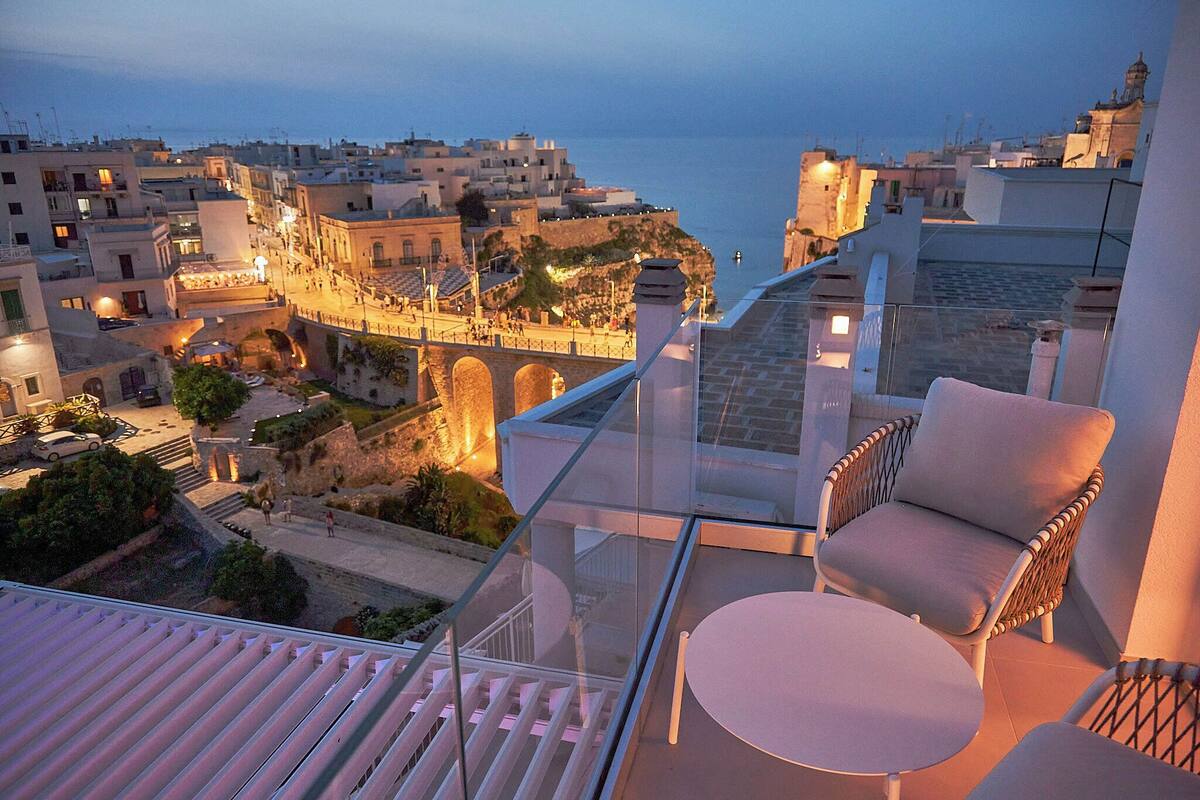 A balcony with a glass railing overlooking a historic town with a view of the sea.