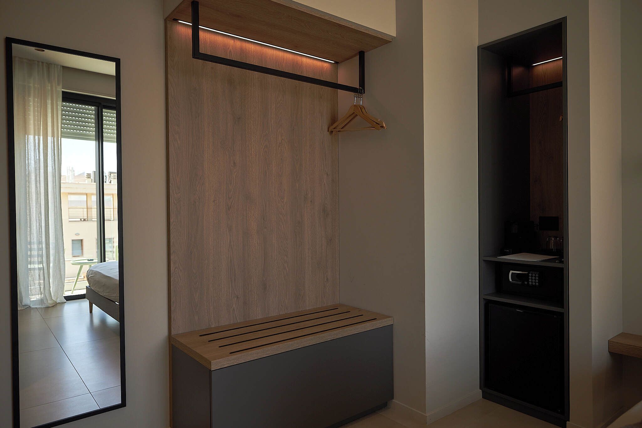A modern bedroom with a wooden bench, a hanging coat rack, and a built-in microwave.