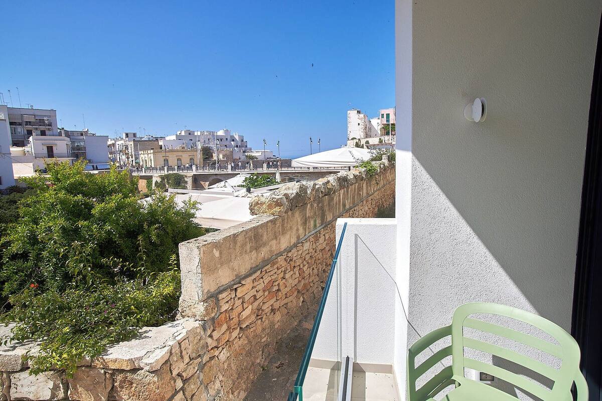 A balcony with a view of a cityscape, stone wall, and greenery.