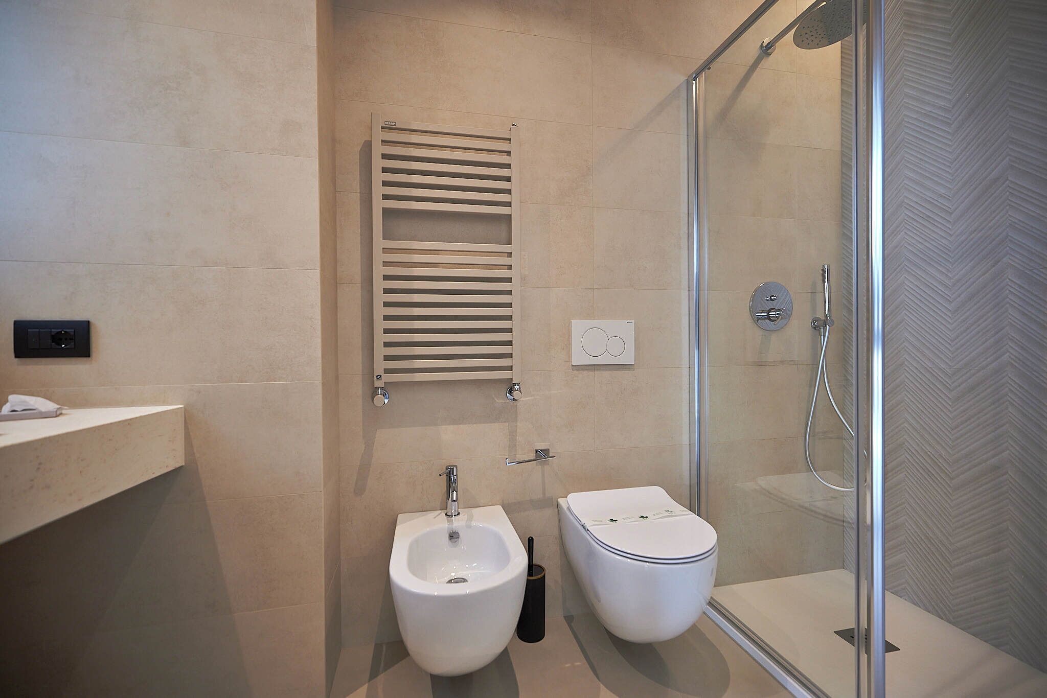 Un baño moderno con bidé, inodoro y ducha con mampara de vidrio.