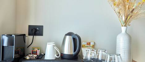 Une table de petit-déjeuner joliment dressée, avec une machine à café, une bouilloire, des tasses et un vase rempli de fleurs séchées.