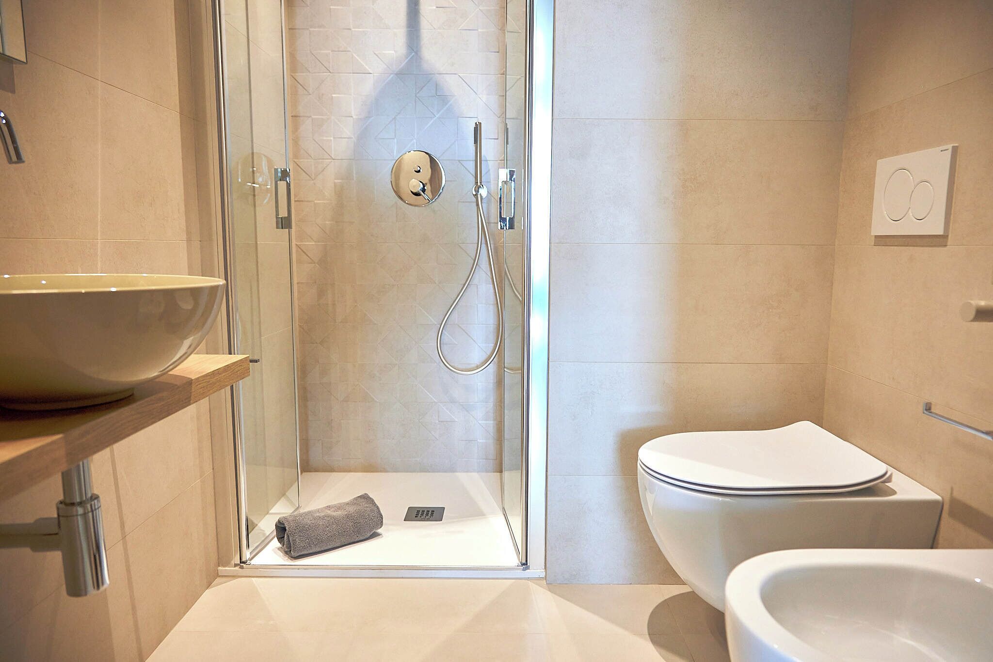 Un baño moderno con ducha acristalada, inodoro blanco y un lavabo grande tipo cuenco.