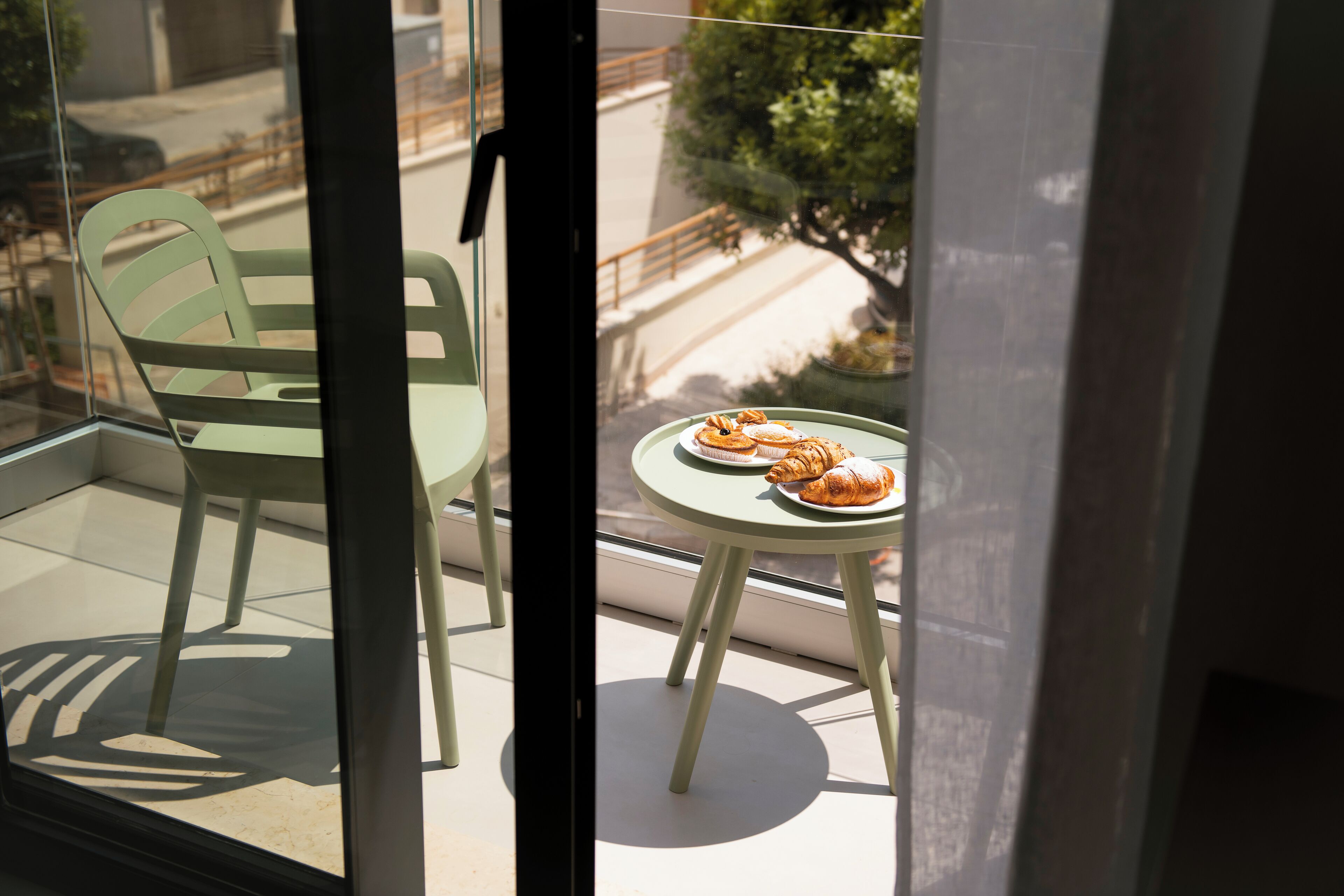 A balcony with a table and chairs, a view of the street, and a tree.