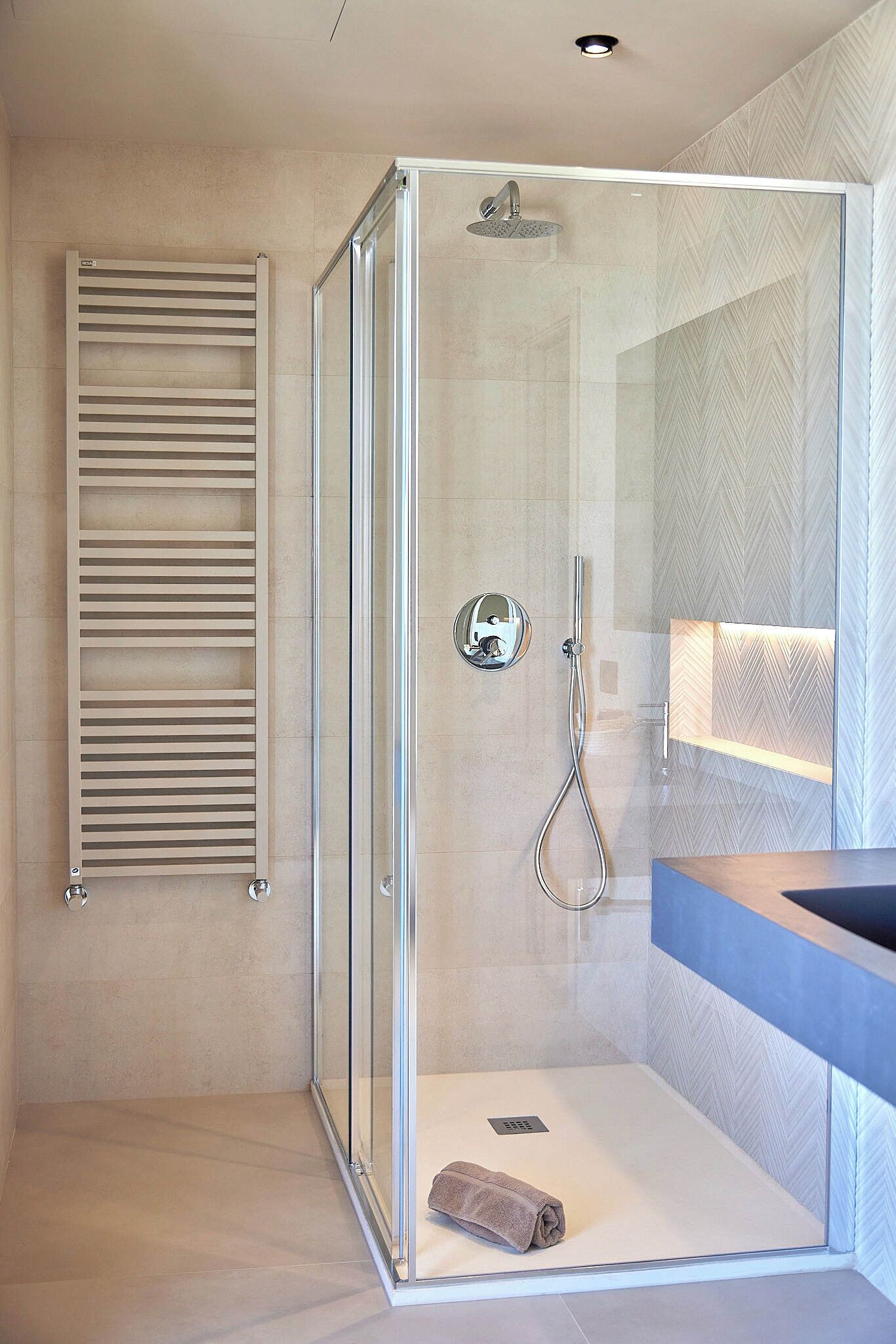 Une salle de bain moderne avec une douche à parois de verre, un porte-serviettes et un meuble-lavabo avec un miroir.