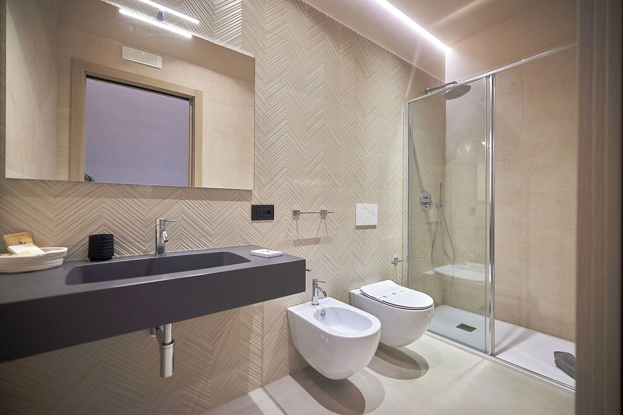 A modern bathroom with a large sink, bidet, and glass shower enclosure.