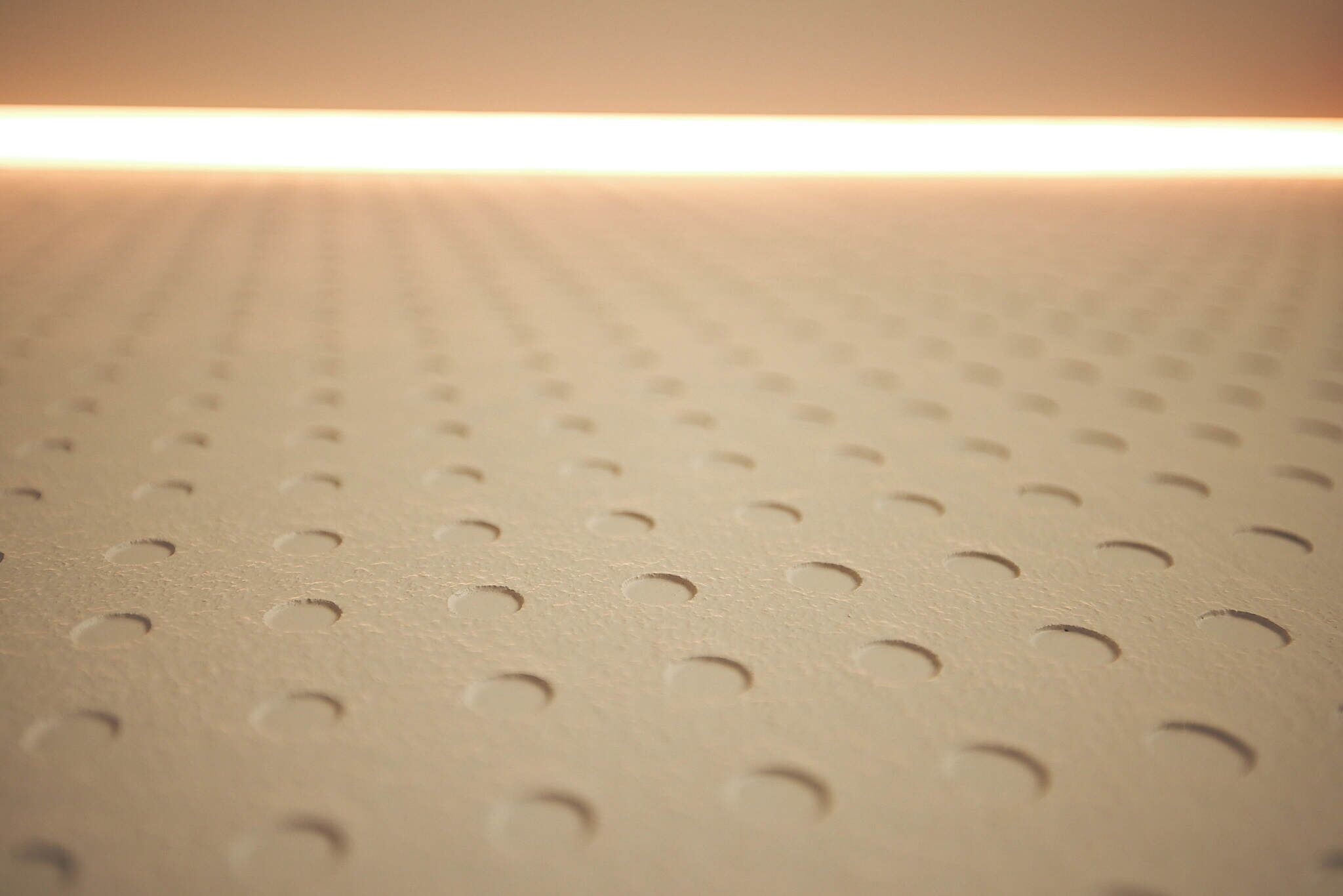 A close-up of a perforated surface with a linear light source in the background.