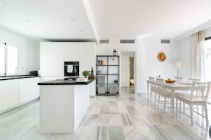 A modern kitchen with a central island, built-in appliances, and a dining area with a table and chairs. - Jardines Puerto Banús – Elegance and Comfort in Marbella’s Heart (Marbella)