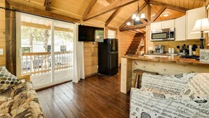 Interior acolhedor de uma cabana com teto de madeira, cozinha com micro-ondas e porta de vidro deslizante que dá para um deck externo.