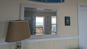 Ein Zimmer mit einem großen Spiegel, einem Schild im Strandstil, einer Lampe und Blick auf den Strand.