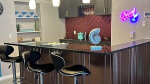 Eine moderne Küche mit Barbereich, ausgestattet mit dunklen Holzschränken, einem Neonlicht und drei Barhocker.