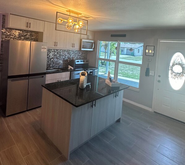 A modern kitchen with stainless steel appliances, a black countertop, and a large window offering a view of the outside.