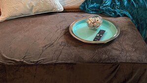 Ein ordentlich bezogenes Bett mit verschiedenen Kissen, einer blauen Decke und einem Tablett mit einer Schale Muscheln und einer Fernbedienung.