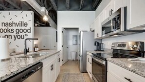 Une cuisine moderne avec des meubles blancs, des plans de travail en granit, des appareils électroménagers en acier inoxydable et un lave-vaisselle apparent.