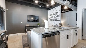 Une cuisine moderne dotée d’un plan de travail en granit, d’un lave-vaisselle en acier inoxydable et d’une pancarte sur laquelle on peut lire : « Nashville vous va à merveille. »