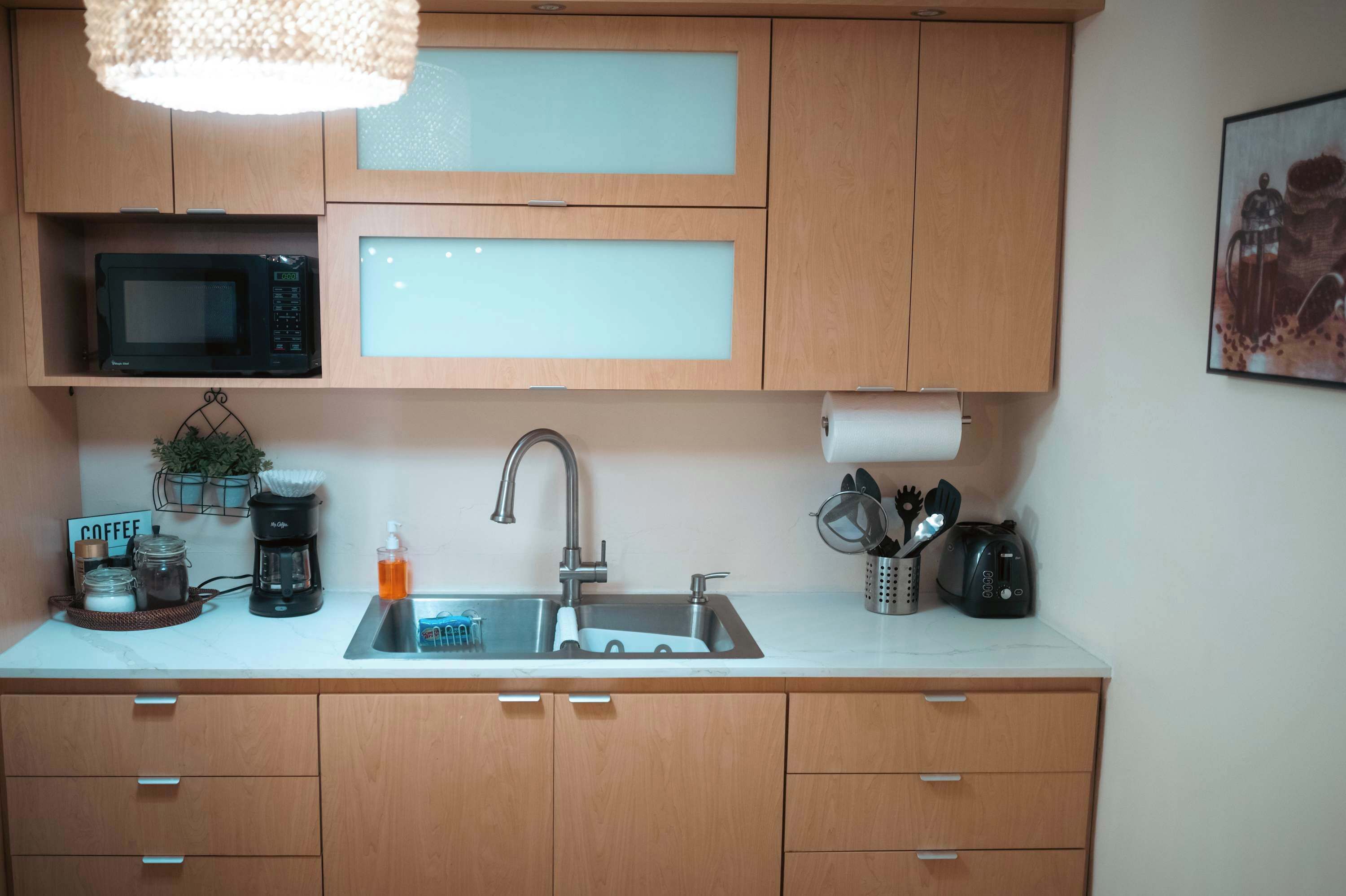 A kitchen with wooden cabinets, a microwave, a coffee maker, and a sink.