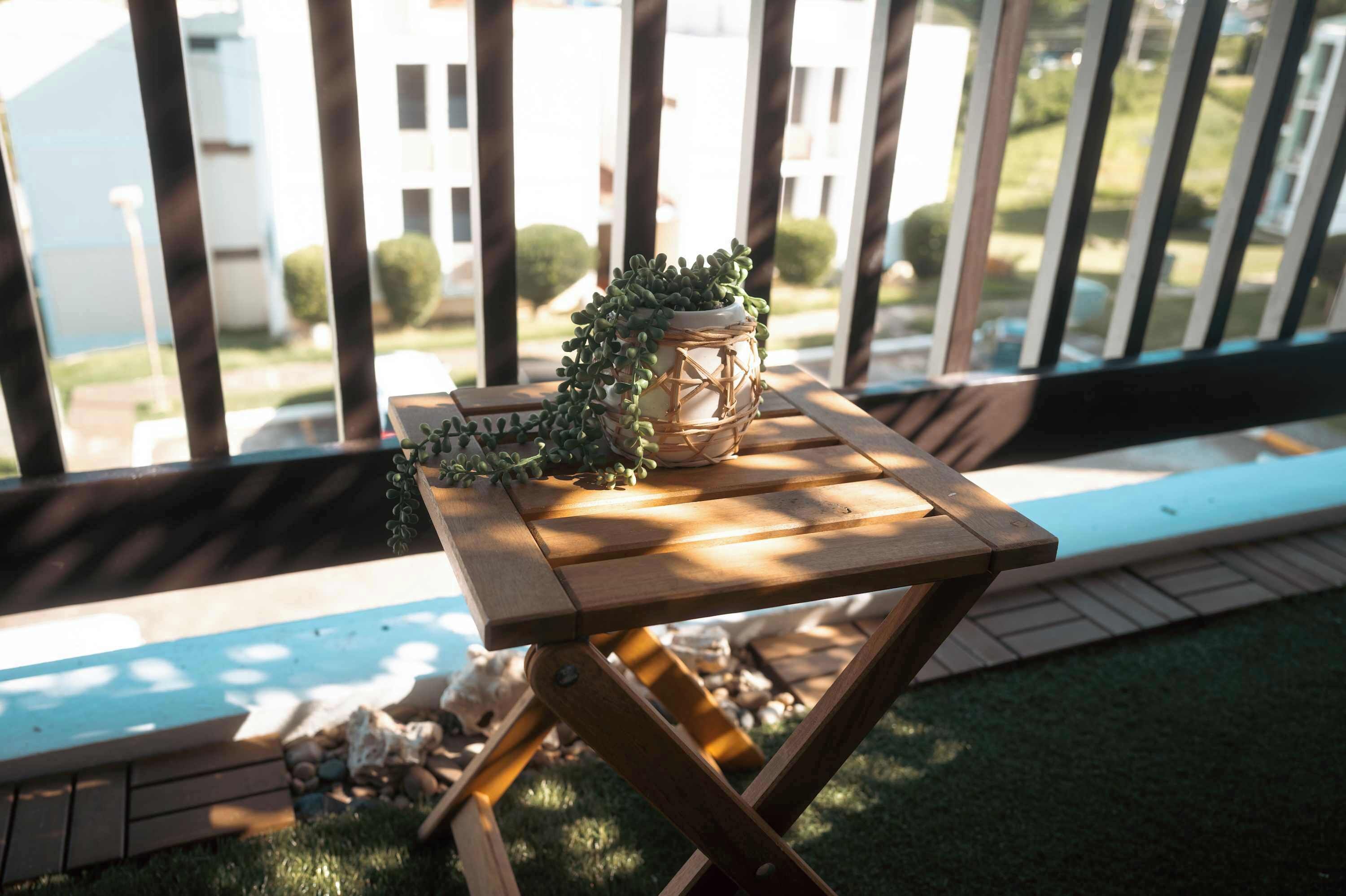 A wooden table with a potted plant on a balcony with a view of residential buildings.