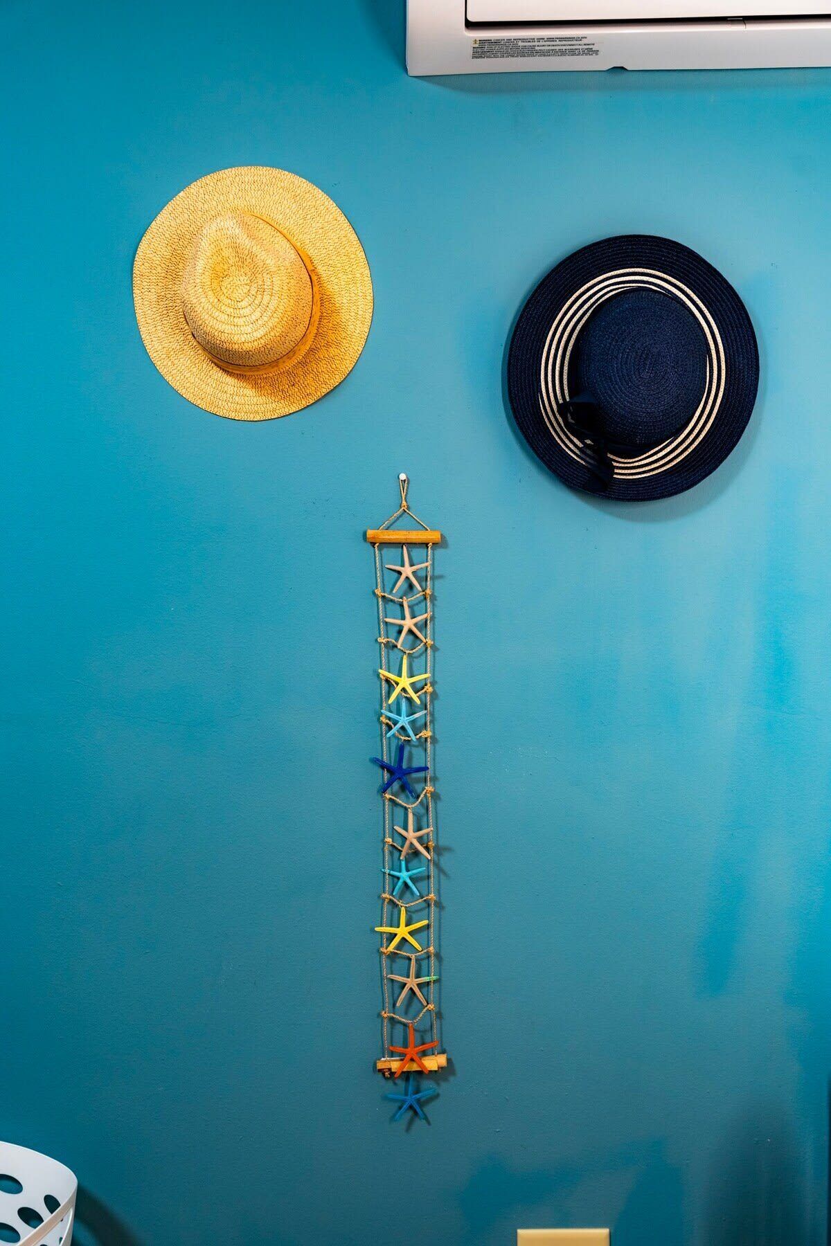 Una pared azul con un sombrero de paja y un sombrero oscuro colgados.
