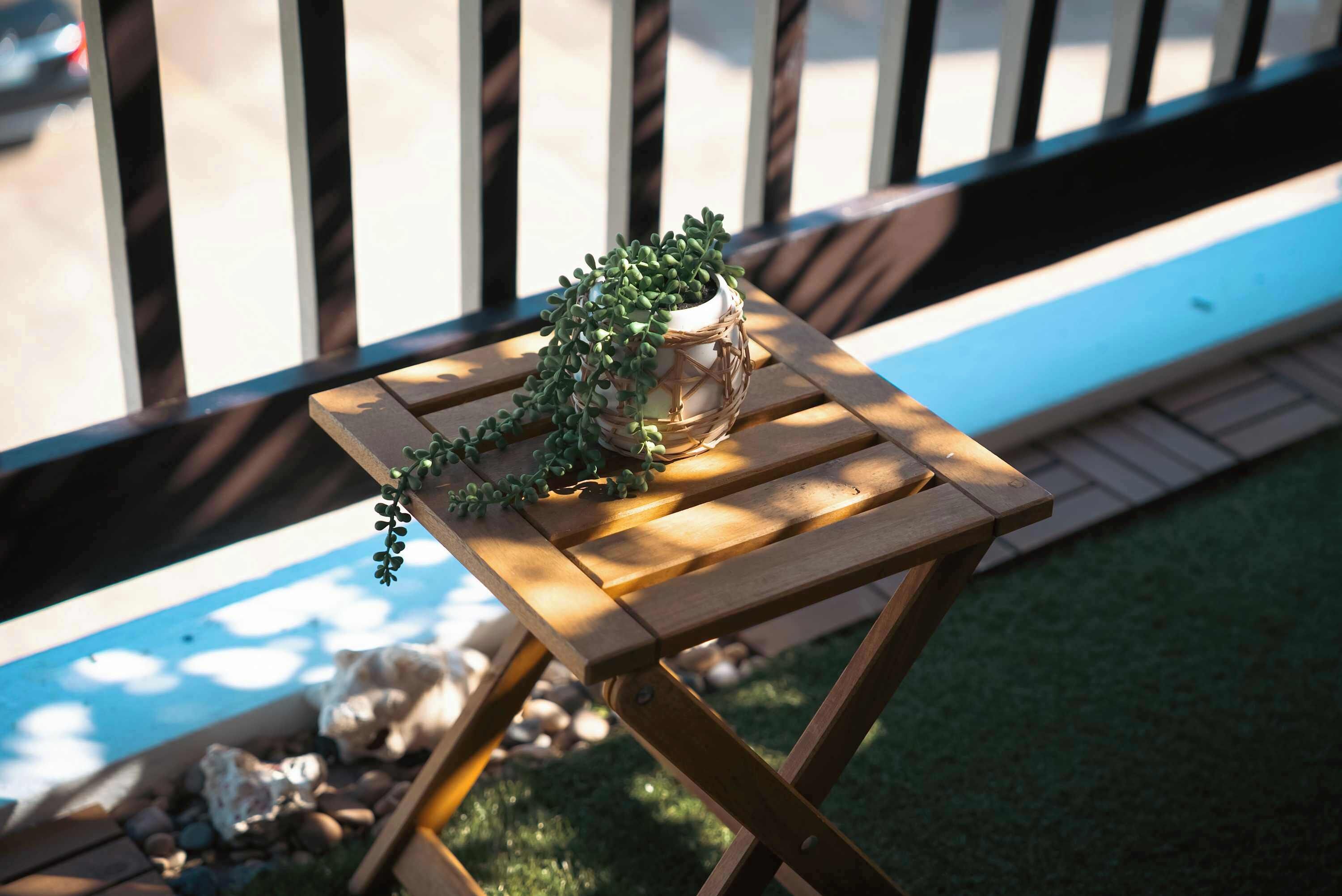 A small wooden table with a potted plant on it, placed on a balcony with a railing.