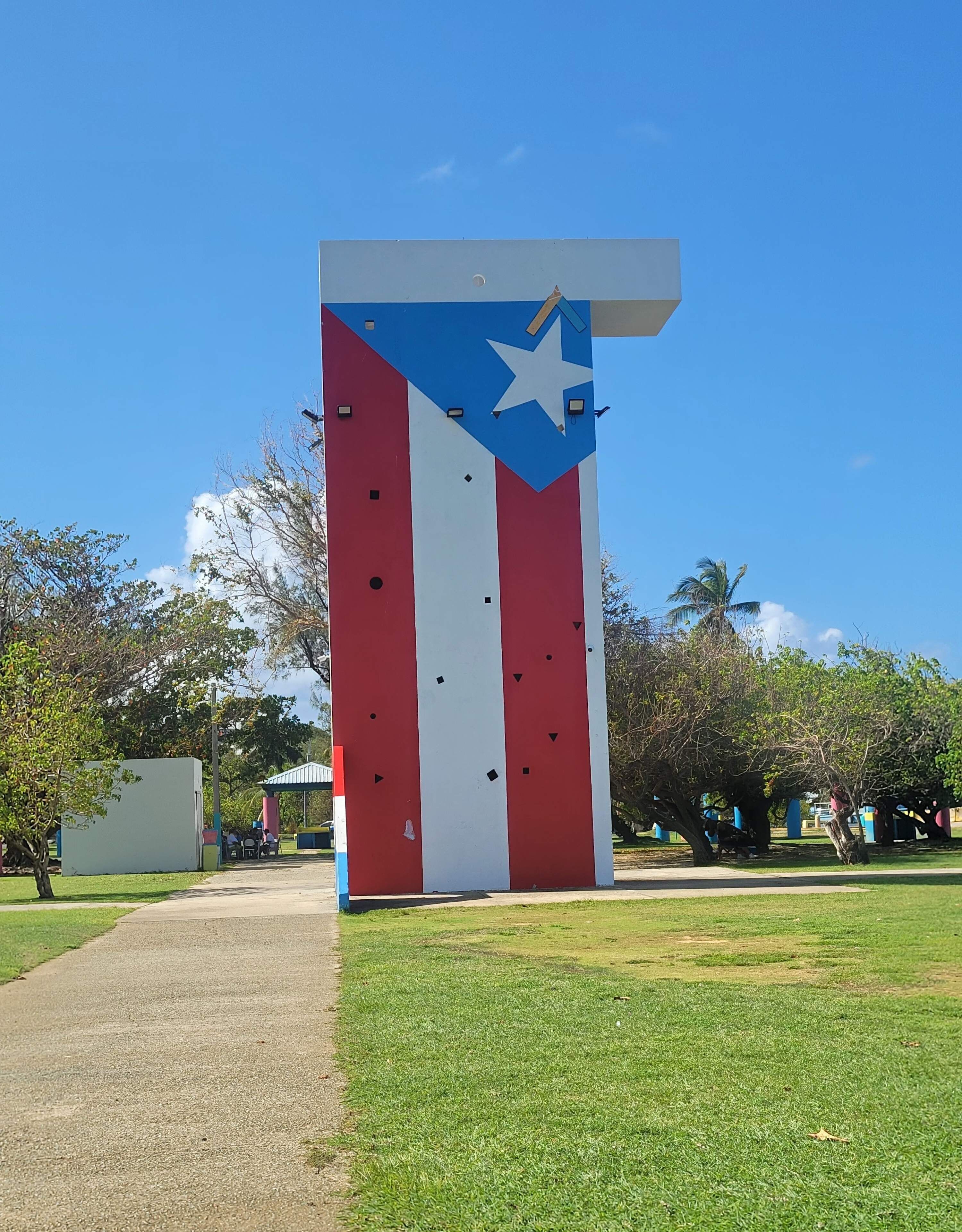 Una estructura alta y vertical con un diseño de bandera, rodeada de hierba y árboles.