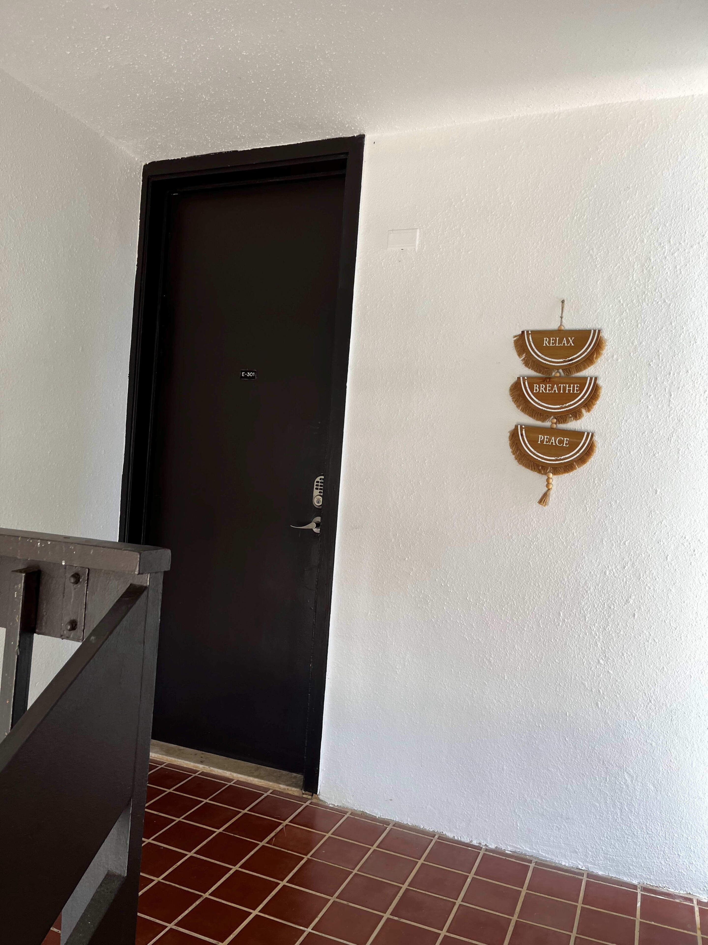 A room with a black door, a white textured wall, and a tiled floor.