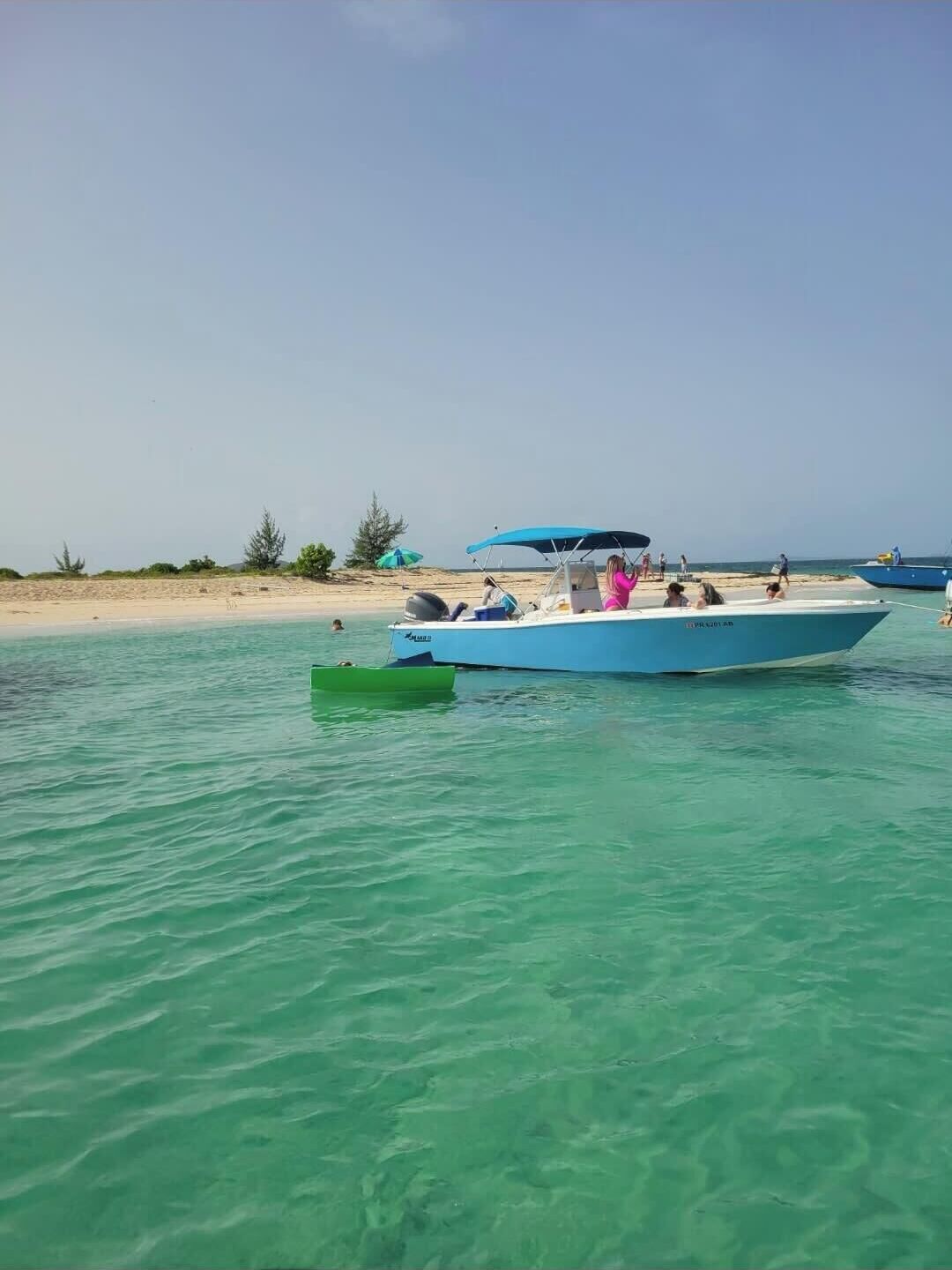 A boat on calm turquoise water with a sandy beach and sparse vegetation in the background.