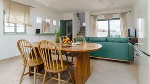 A modern living room with a wooden dining table, green sofa, and a TV.