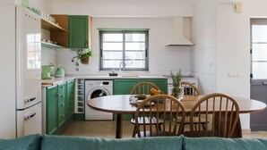 A compact kitchen with green cabinets, a dining table with chairs, a washing machine, and a window with a view.