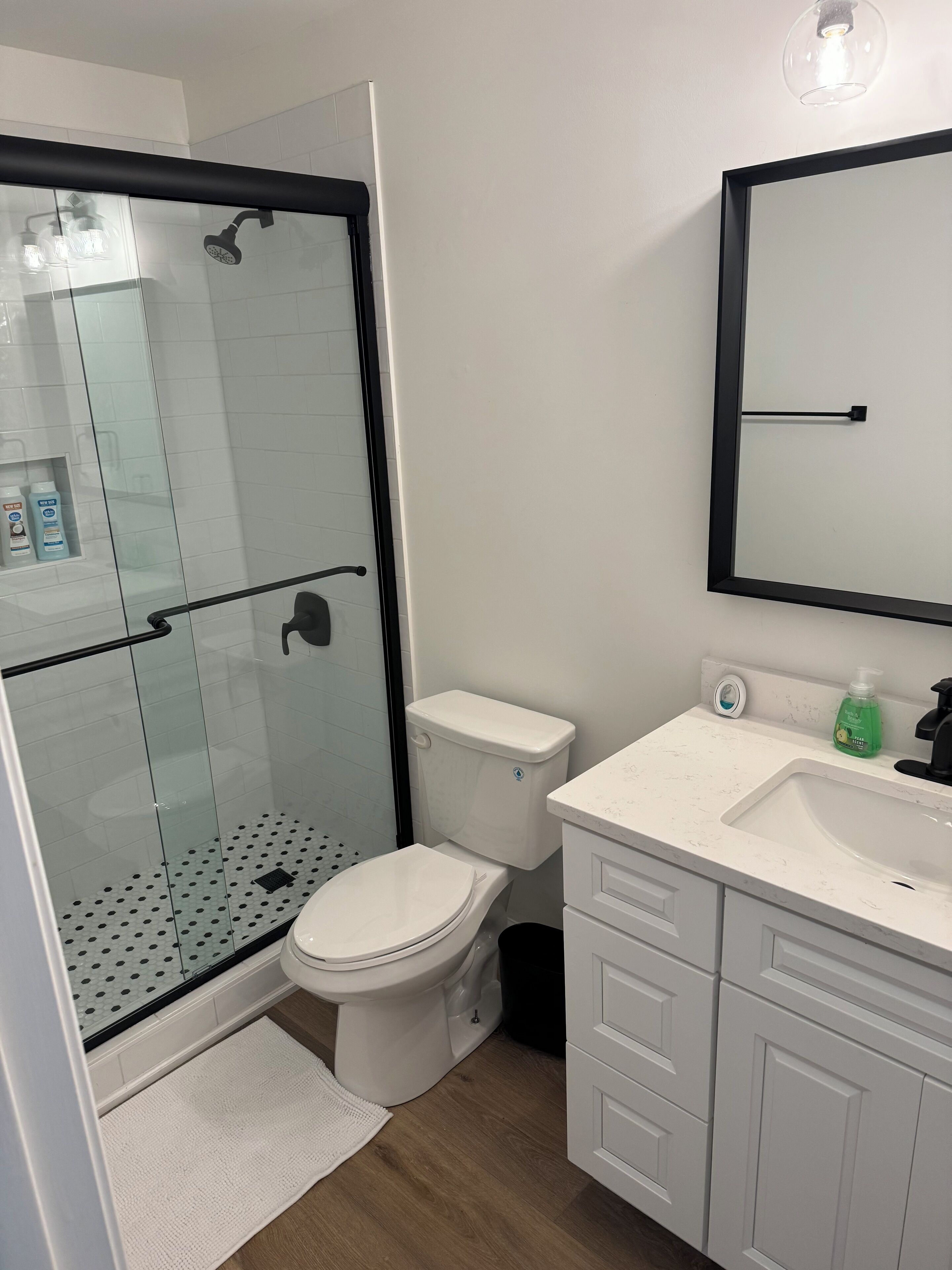 Een moderne badkamer met een douchecabine van glas, een wit toilet en een wastafel met spiegel erboven.