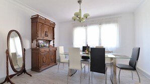 Un coin repas comprenant une table à plateau en verre, quatre chaises, un meuble en bois et un grand miroir.