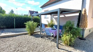 Un espace extérieur abrité, aménagé avec une table et des chaises, entouré de gravier et de petites plantes.
