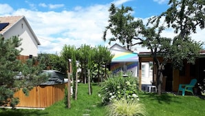 Un jardin à l’arrière de la maison, avec une clôture en bois, un jacuzzi et un espace planté de différentes espèces végétales, ainsi qu’une fresque murale représentant un arc-en-ciel.