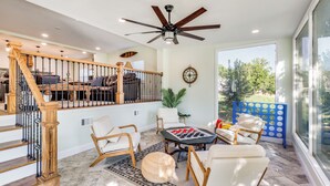 A spacious living area with a wooden staircase, a ceiling fan, and a large window offering a view of the outdoors. - The Falling Pecan Lakehouse  (Granbury)