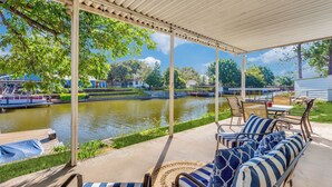 A covered patio with outdoor furniture, a view of a water body, and surrounding greenery. - The Falling Pecan Lakehouse  (Granbury)