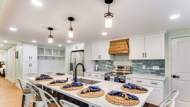 A modern kitchen with white cabinets, a large island with stools, stainless steel appliances, and pendant lighting. - The Falling Pecan Lakehouse  (Granbury)
