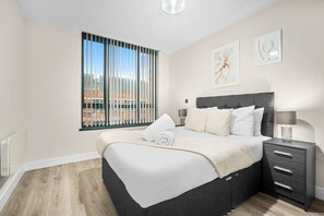 A modern bedroom with a large bed, bedside tables, and a window with blinds.