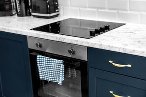 A kitchen with a black induction cooktop, a built-in oven, and a marble countertop.