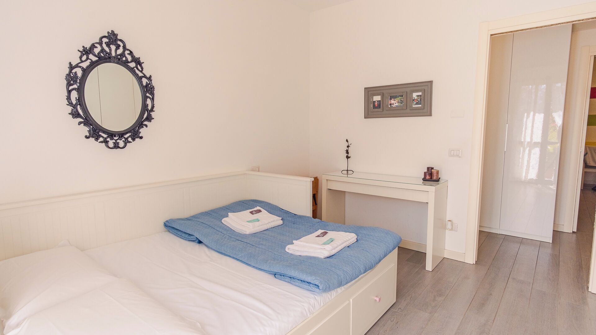 Een slaapkamer met een bed, nachtkastje, spiegel en een klein bureau.