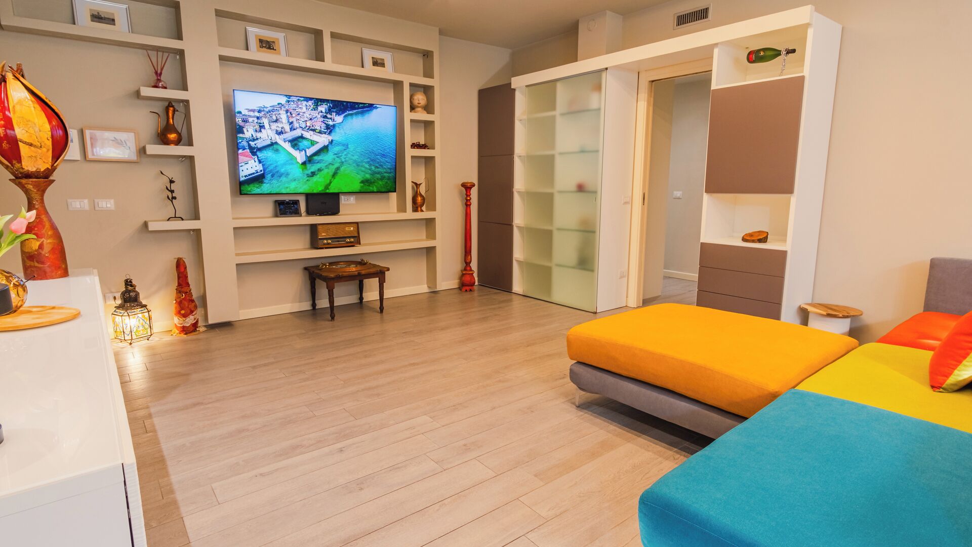 A modern living room with a flat-screen TV, wooden flooring, a sofa, and a sliding glass door closet.