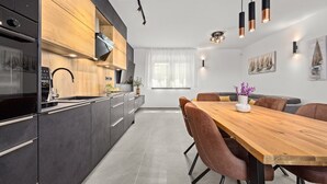 A modern kitchen with dark cabinetry, a wooden countertop, and a built-in oven. There is a dining area with a wooden table and leather chairs. - Villa Antares - Luxurious Vacation Oasis (Štinjan)