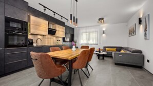 A modern kitchen with dark cabinetry, a wooden dining table, and brown upholstered chairs. - Villa Antares - Luxurious Vacation Oasis (Štinjan)