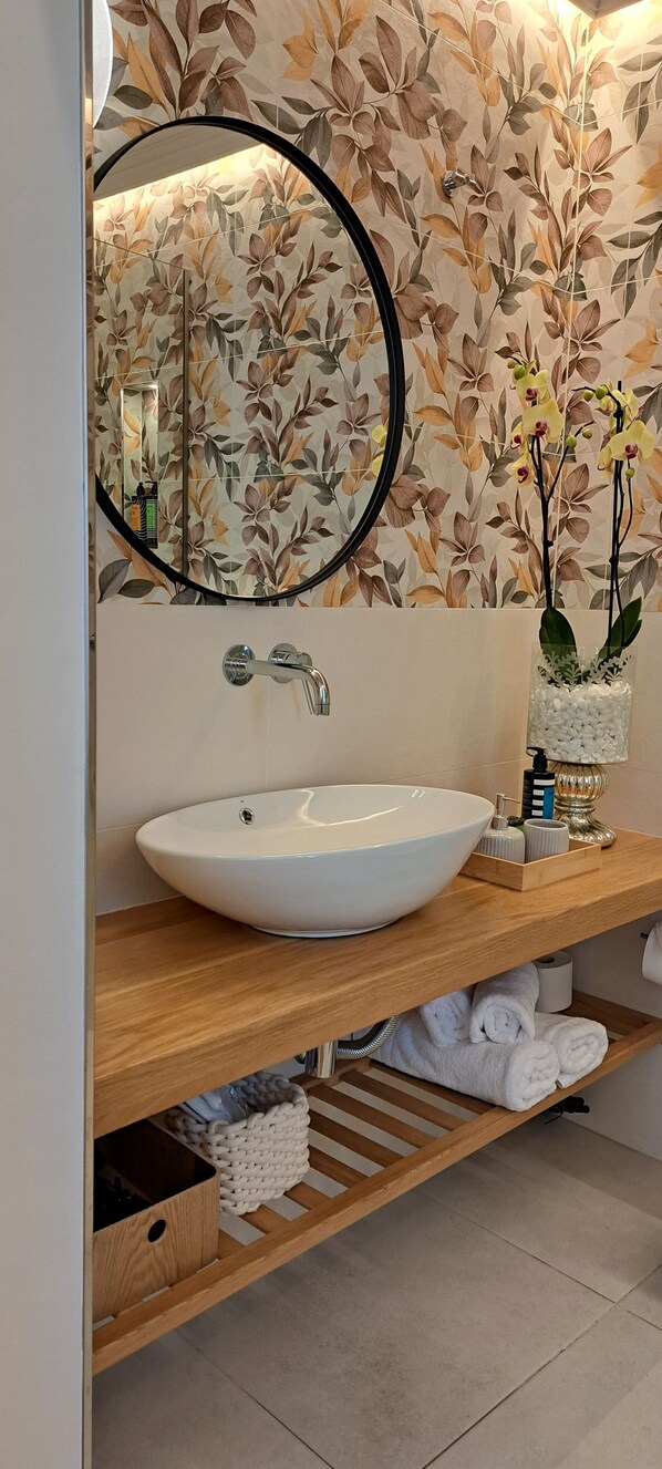 Une salle de bain avec un lavabo blanc, un miroir et un papier peint à motifs floraux.