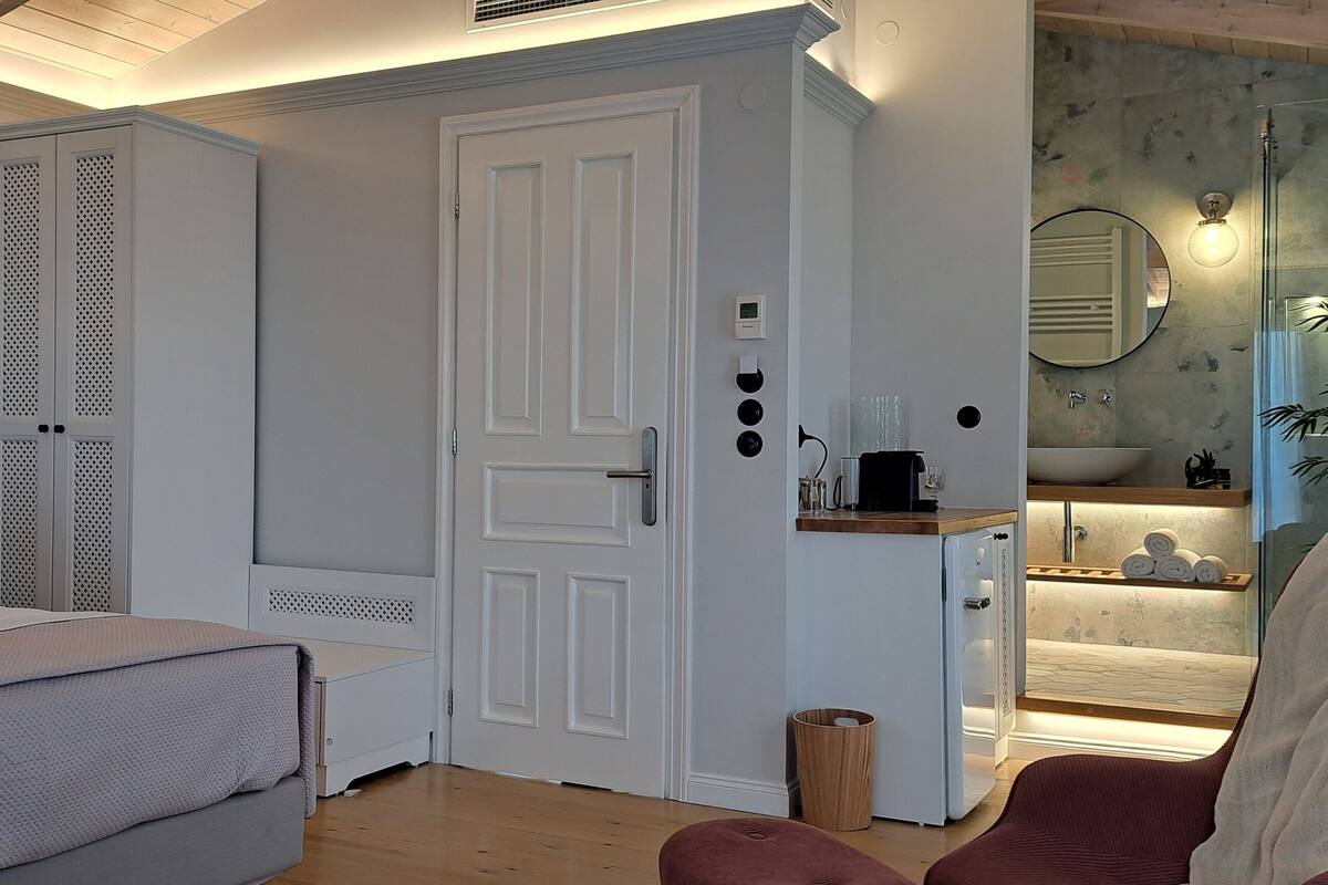A bedroom with a bed, a wardrobe, a bathroom with a sink and mirror, and a chair.