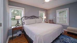 A bedroom with a bed, two bedside tables with lamps, a ceiling fan, and a window with blinds. - Johnson Street Cottage in Downtown Brevard (Brevard)