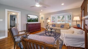 A living room with a sofa, armchair, coffee table, and a TV mounted on the wall. - Johnson Street Cottage in Downtown Brevard (Brevard)