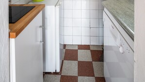Cocina compacta con azulejos blancos, cafetera, pileta y ventana.