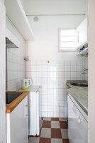 Una cucina compatta rivestita di piastrelle bianche, con macchina da caffè, lavandino e finestra.