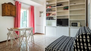 Una habitación con una mesa de comedor y sillas, una estantería, un sofá y una televisión.