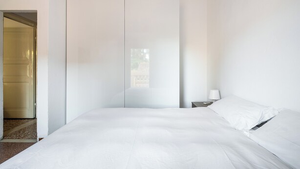 Un dormitorio minimalista con una cama grande, un armario y una mesita de noche con una lámpara.