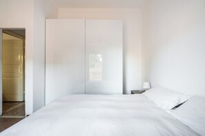 Un dormitorio minimalista con una cama grande, un armario y una mesita de noche con una lámpara.